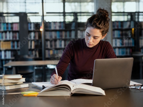 Student studying in library with laptop books and handwritten notes