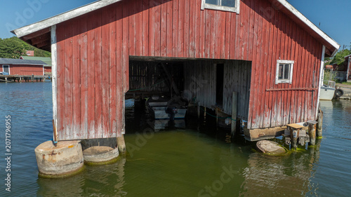 Aerial view of a red wooden boathouse in Rosala, featuring weathered timber walls and a small boat moored inside over calm water Kimitoon, Southwest Finland, Finland.