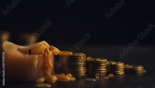 Melted candle with stacked gold coins on dark background, symbolizing savings and wealth