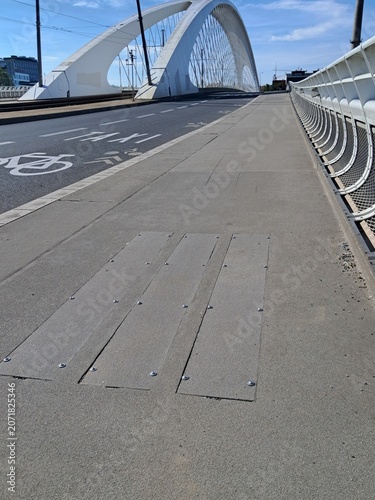 Rectangular asphalt service covers and access hatches for infrastructure communications on a pedestrian sidewalk of the Troja Bridge in Prague.