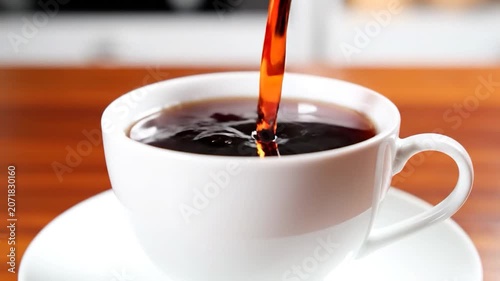 Fresh hot tea is poured into a white ceramic cup on a wooden table