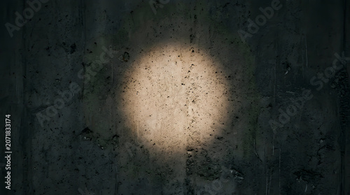 Circular spotlight illuminating a gritty dark concrete wall surface for industrial background design