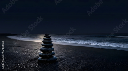 Stacked zen stones on a dark sandy beach at night with gentle ocean waves under dim moonlight