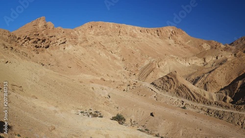 PAN: Rugged phosphate-rich mountains rise from the arid landscape near Chebika, Tunisia, revealing layered rock formations, desert geology, and vast open terrain beneath a clear blue sky