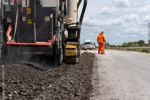 Bild auf Leinwand Heavy asphalt milling machine removing old pavement during road construction work with an unrecognizable worker in the background