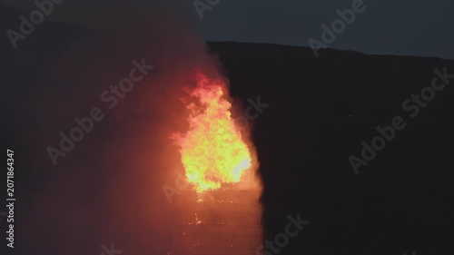 ALESUND, NORWAY, JUNE 20, 2026. Slinningsbalet burns brightly beside the sea in Alesund, Norway, a towering midsummer bonfire reflecting fiery light on dark water on a summer night