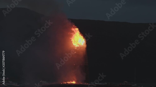 ALESUND, NORWAY, JUNE 20, 2026. Slinningsbalet burns brightly beside the sea in Alesund, Norway, a towering midsummer bonfire reflecting fiery light on dark water on a summer night