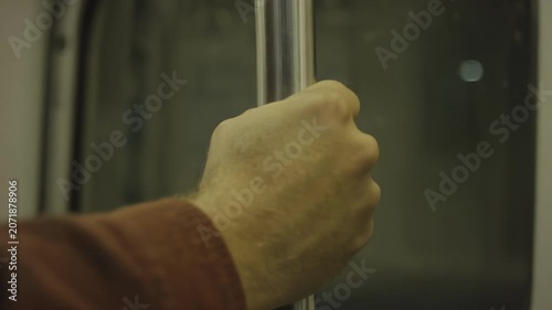 Hand gripping a metal pole inside a subway train, showcasing the steady hold as the train moves through a dimly lit tunnel with reflections on the glass