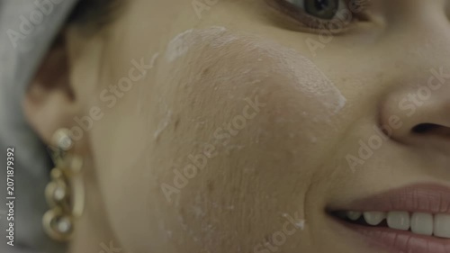 Woman applying facial cream to her cheek in a close-up shot, showcasing the gradual spreading of the product across her skin with a soft focus background
