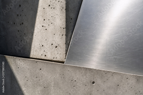 Abstract architectural background featuring geometric concrete panels and brushed metal surfaces with dramatic natural light and shadows. Minimalist industrial composition showcasing raw materials.