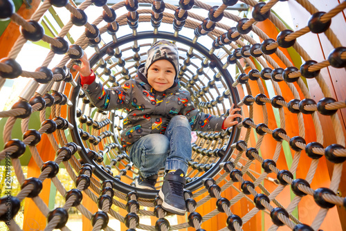 Child plays in a playground structure made of ropes and wood in a sunny outdoor setting during the day