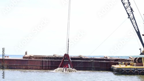 Water drains from the scoop of a dredging crane as it is lifted from the water
