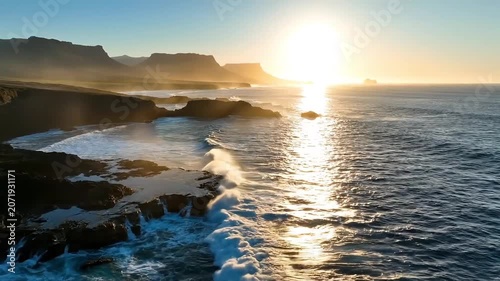 Golden sunbeams illuminate crashing ocean waves against rugged coastal cliffs at sunrise.
