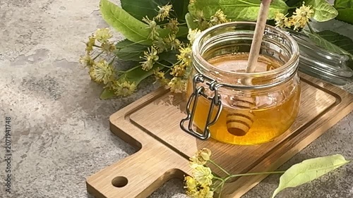Fresh linden honey in glass jar with dipper and blossoms
