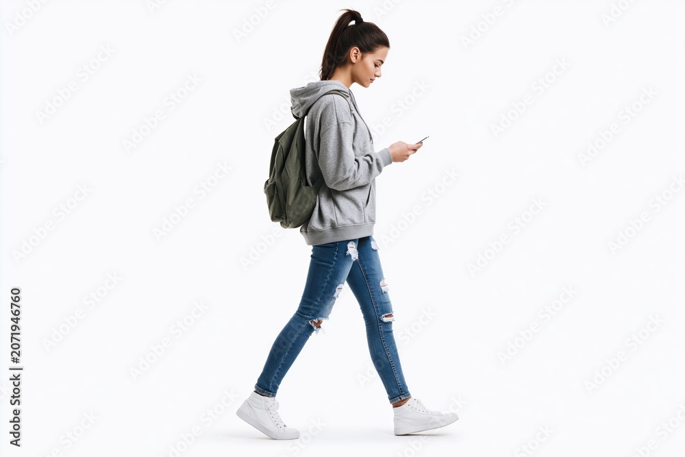 Obraz premium Student woman walking with a backpack and smartphone isolated on white background