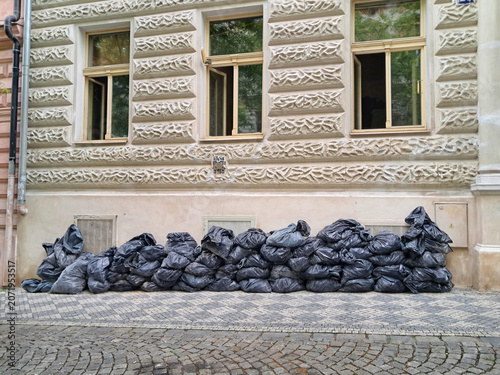 A straight front view of a long row of black plastic bags filled with construction waste stacked against a historic building facade in Prague.