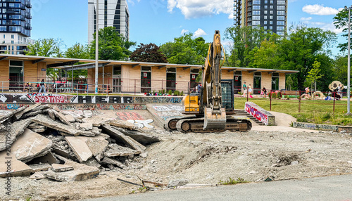 Construction work takes place at a park area with a skating ramp in a city