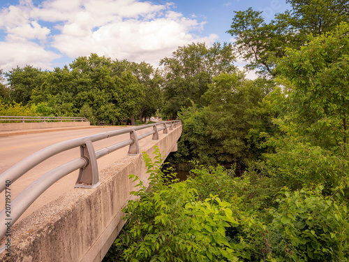 Konstfotografi Concrete road bridge with metal guardrails crossing over a river surrounded by l