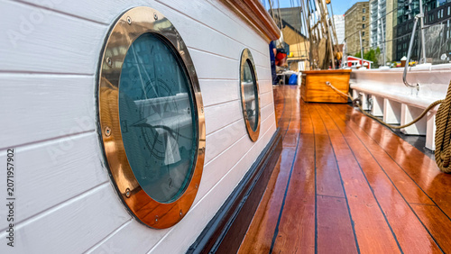 Bild auf Leinwand Wooden deck of a boat with round porthole and city buildings in background