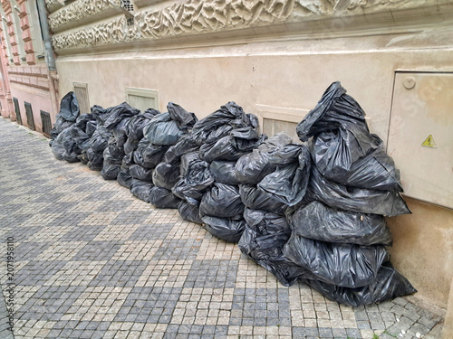 An angled perspective view of multiple black plastic trash bags full of demolition debris left on a paved sidewalk in Prague.