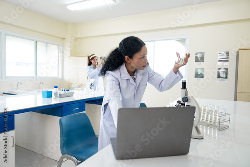 African American female scientist working with microscope and notebook computer in laboratory