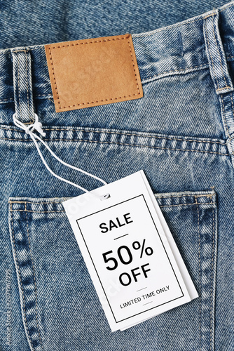 Jeans label closeup with discount tag. Fifty percent sale promotion on denim clothing. Retail shopping campaign and seasonal fashion offer. Store marketing background.