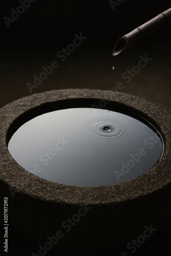 Serene dark background highlighting a bamboo fountain dripping into a calm rock pool