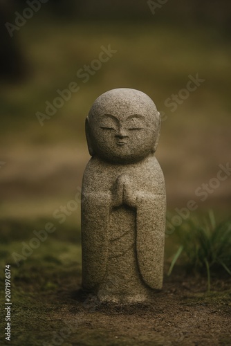 Small stone jizo statue standing peacefully in a traditional zen garden setting
