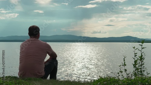 A lonely man sits on the shore of a lake and admires the beauty of nature, drawing inspiration and peace. Harmony of nature and man. Alone with myself.