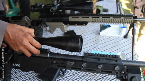 A close up view of precision rifles equipped with optical scopes during a firearms display, highlighting advanced shooting equipment, tactical technology, and marksmanship training.