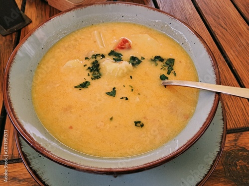 A close up top view of a hot bowl of traditional Czech sauerkraut soup, known as Zelnacka, garnished with fresh herbs on a wooden table.