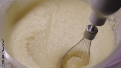 Close-up, hand mixer whipping buttercream in plastic bowl