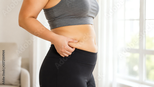 A woman examines her body in casual wear, focusing on self-acceptance and body positivity in a modern living room setting.