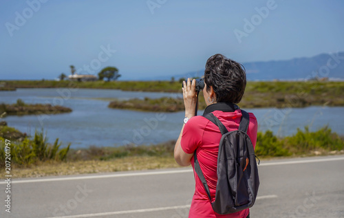 Canvas Print Woman observing wildlife with binoculars next to the lagoon