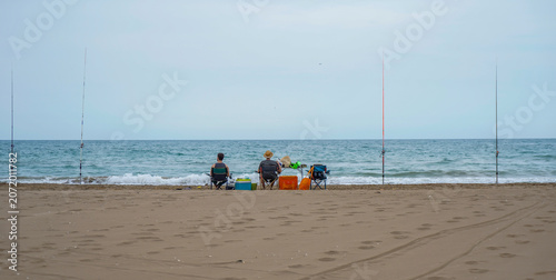 Canvastavla Two people fishing sitting on the seashore