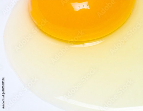 Cracked Fresh Chicken Egg with Golden Yolk Flowing on White Surface