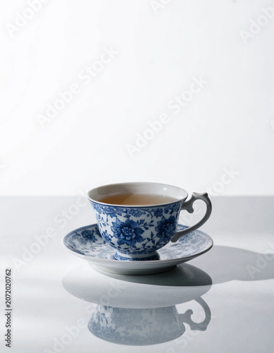 Vintage blue and white floral porcelain teacup with matching saucer on a reflective surface