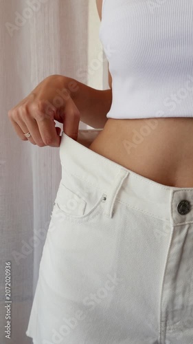Woman showing loose-fitting jeans after weight loss and body transformation.