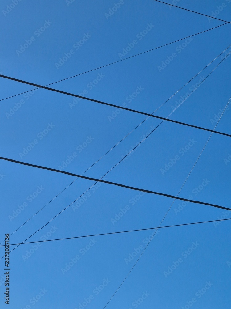 Fototapeta premium Black Power Lines Crossing Clear Blue Sky Background