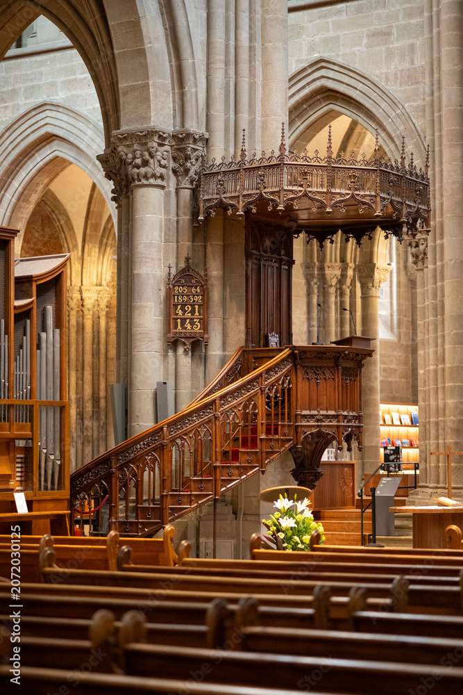 Naklejka premium Gothic Cathedral Interior with Ornate Wooden Pulpit, Pipe Organ and Stone Arches, Geneva Switzerland - A grand interior view of a Gothic cathedral. St. Pierre's Cathedral in Geneva.