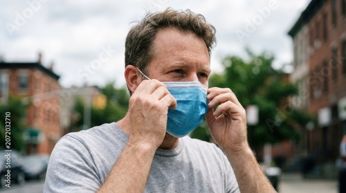 Man adjusting blue surgical mask outdoors in city.