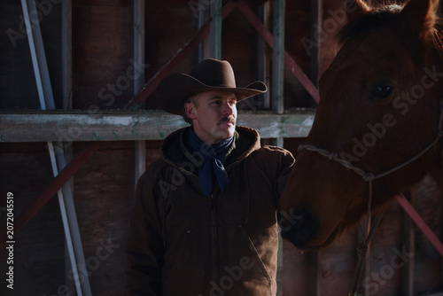 Cowboy interacts with horse inside barn during daylight hours