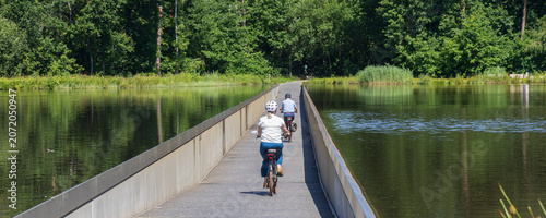 Couple cycling across narrow causeway through a lake in Bokrijk park near Genk, Flanders in Belgium