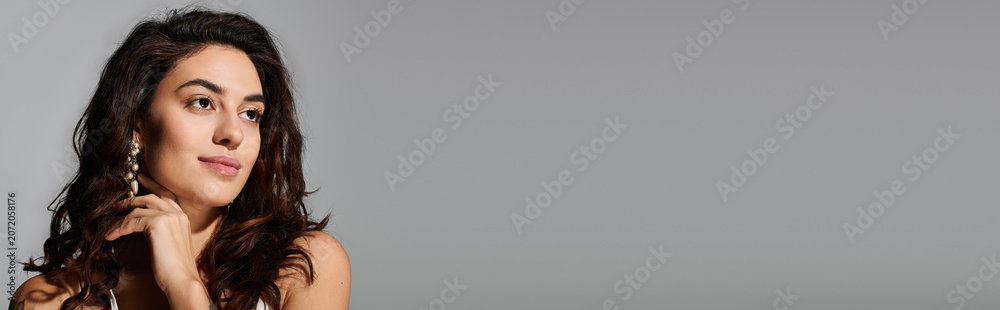 Naklejka premium Beautiful young woman showcases her style with elegant earrings in a simple background.