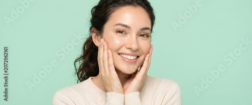 Young woman with healthy glowing skin touching her cheeks, isolated on a light mint green background