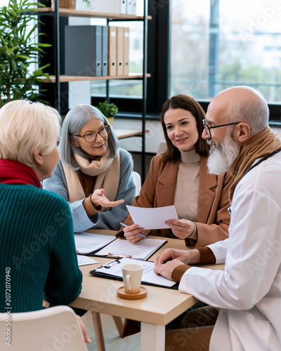 Senior patients consulting with healthcare professionals during medical meeting discussing treatment options insurance coverage and care planning in modern clinic environment