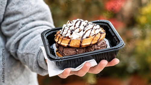 Hand holding black tray with waffle dessert topped with ice cream and