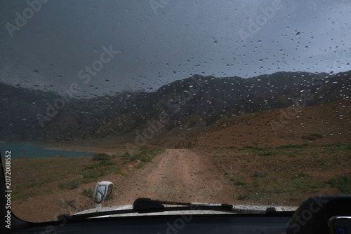 Driving in rain on remote dirt road view from interior. Commercial background for travel, auto adventure, off-road lifestyle, car insurance and stormy weather concepts with copy space.
