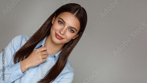 Professional woman confidently adjusting her light blue button down shirt collar in a soft studio lighting environment for corporate branding