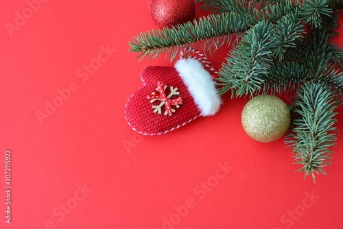 Christmas background with fir branches, red and gold ornaments, and a mitten on a red surface